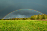 Rainbow on a background of clouds over the forest and meadow