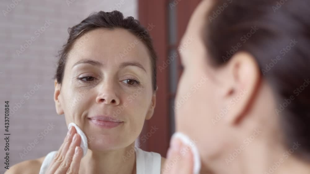 Smooth natural woman skin. A woman with a pad takes off her make up by the mirror in the room. Smooth natural woman skin. A woman with a pad takes off her make up by the mirror in the room.