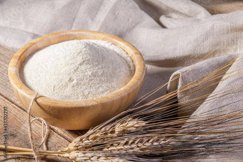Foto Whole wheat durum flour in wooden bowl with spikelets on a natural wooden backgr