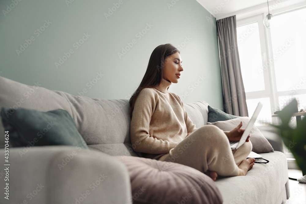 Young woman using laptop, sitting on couch at home, beautiful girl shopping or chatting online in social network, having fun, watching movie, freelancer working. Young woman using laptop, sitting on couch at home, beautiful girl shopping or chatting online in social network, having fun, watching movie, freelancer working.