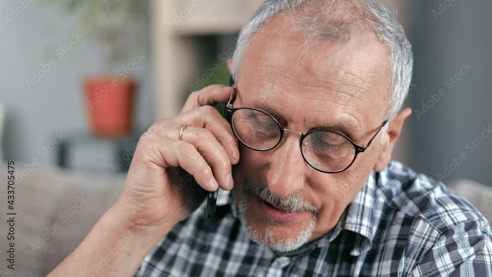 Closeup face elderly 70s man talking smartphone calling to doctor clinic sitting on couch at home Closeup face elderly 70s man talking smartphone calling to doctor clinic sitting on couch at home
