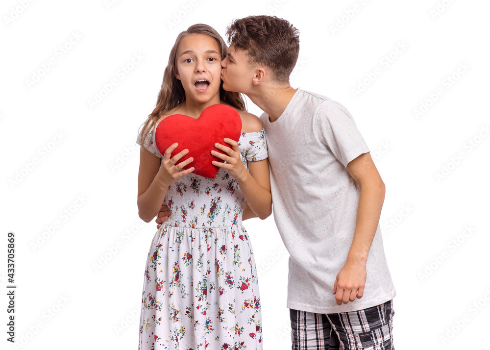 Portrait of sweet young teenagers couple in love - first kiss. Teen girl holds plush heart in hands. Teen boy kissing teen girl. Friendship and love concept