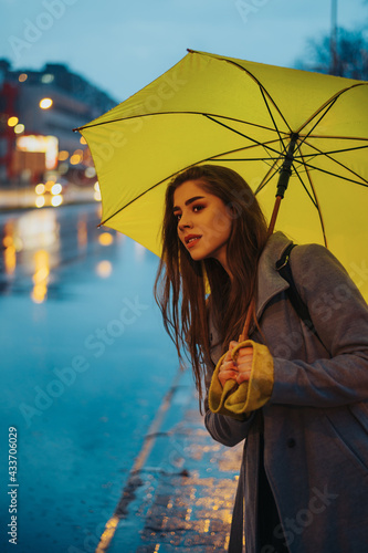 Young beautiful woman holding a yellow umbrella and waiting for a cab on a rainy night