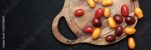 Plum Cherry On White Round Cutting Board. Assorted Plump Cherry Tomatoes On Wooden Cutting Board. Scattered Red, Yellow And Black Plum Cherry Tomato On Black Grunge Background.