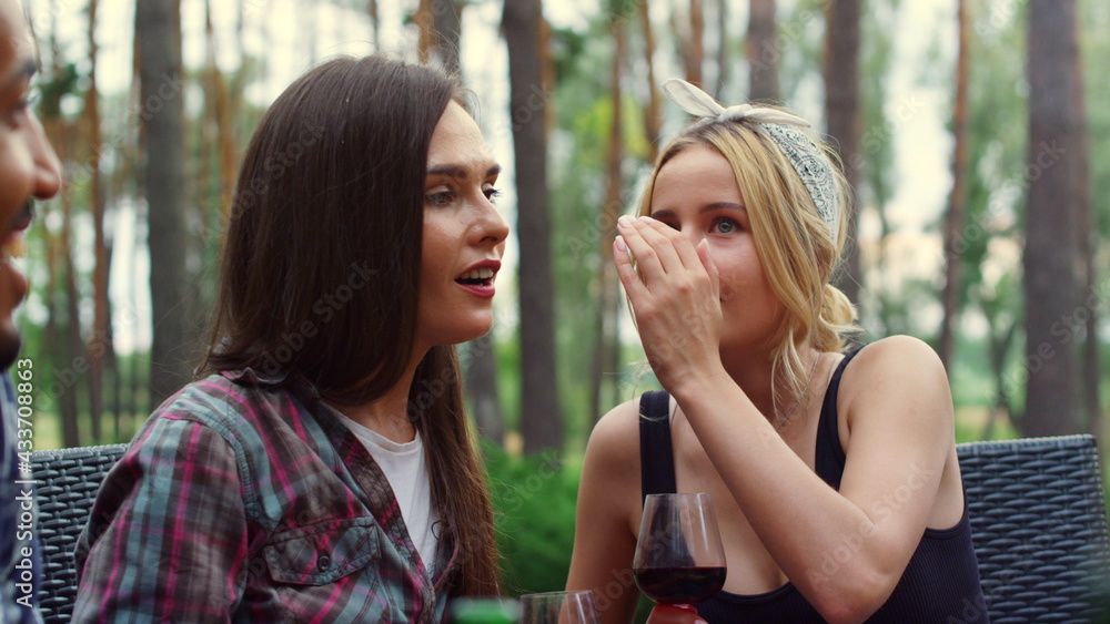 Young women sharing secrets on backyard. Girls chatting on party outdoors Young women sharing secrets on backyard. Girls chatting on party outdoors