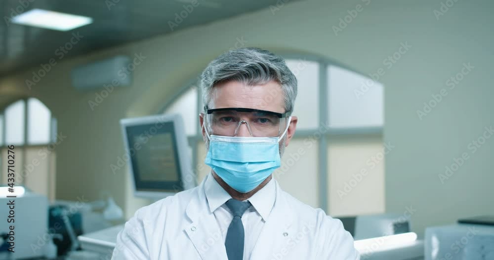 Close up portrait of cheerful positive Caucasian bearded male professional medic in medical mask standing in clinic laboratory looking at camera and smiling. Hospital lab, coronavirus pandemic Close up portrait of cheerful positive Caucasian bearded male professional medic in medical mask standing in clinic laboratory looking at camera and smiling. Hospital lab, coronavirus pandemic