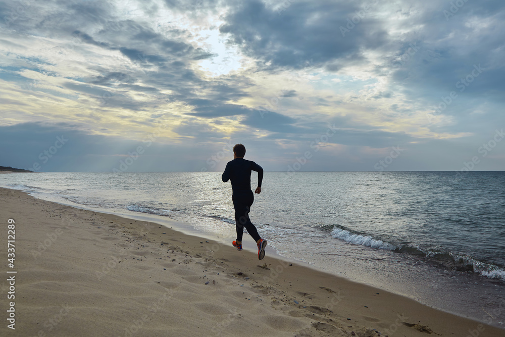 Young man in sports outfit runs along the seashore Young man in sports outfit runs along the seashore