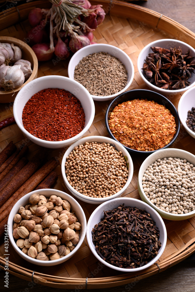 Various dry spices and herbs in a bowl on bamboo tray. Asian food ingredients (chili, clove, caraway, coriander seed, star anise, cardamom, pepper, cinnamon, garlic and shallot)