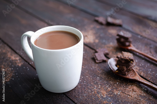 Chocolate milk in white cup with bar chocolate in spoon on wooden table background. coco hot drink in the morning for health. World Chocolate Day and snack or breakfast concept.