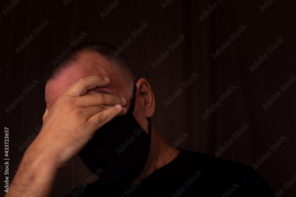 White latin man with black mask and black T-shirt holding his forehead with his hands. Concept of sadness White latin man with black mask and black T-shirt holding his forehead with his hands. Concept of sadness