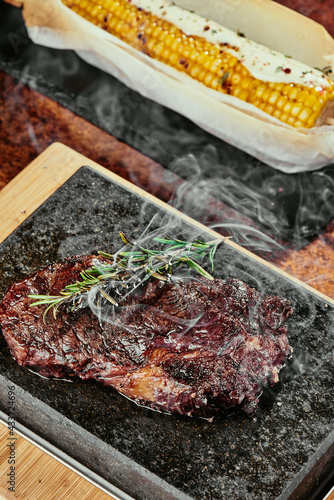 Fermented steak. Steak with rosemary on a black plate served with grilled corn on a background of greens, spices and fresh vegetables, on a copper sheet