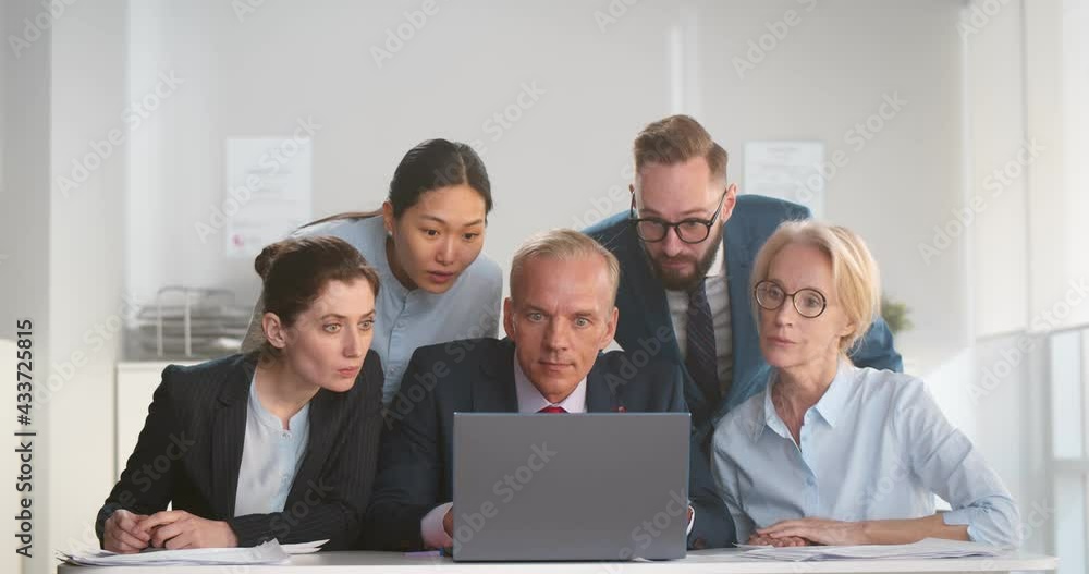 Multiethnic business team looking at laptop screen while working together in office Multiethnic business team looking at laptop screen while working together in office