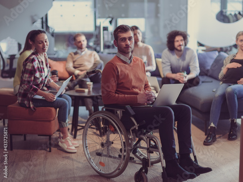 Disabled businessman in a wheelchair at work in modern open space coworking office with team