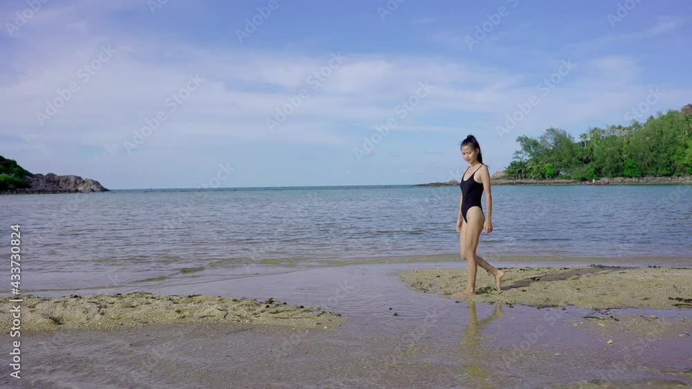 Young Pretty Asian Woman in Black Swimsuit Walking Alone on a Sandbar, in Slow Motion, Thailand. Young Pretty Asian Woman in Black Swimsuit Walking Alone on a Sandbar, in Slow Motion, Thailand.