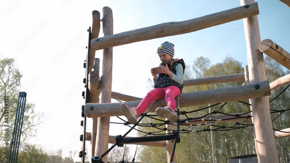Child Girl Chooses Gadget Instead of Active Games, Playing Games on a Smartphone while Sitting in Playground. Internet Addiction and Electronic Devices Concept Child Girl Chooses Gadget Instead of Active Games, Playing Games on a Smartphone while Sitting in Playground. Internet Addiction and Electronic Devices Concept