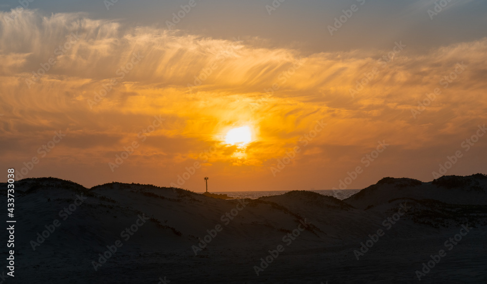 Orange sunset silhouette on the beach with clouds and sand dunes