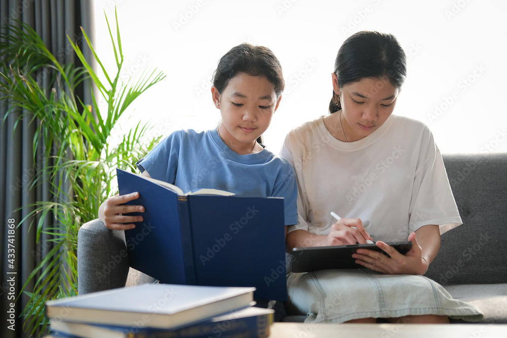 Obraz premium Two young asian girls sitting on sofa and using digital tablet together.