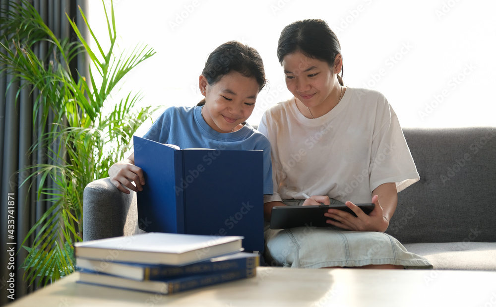 Obraz premium Two young asian girls sitting on sofa and using digital tablet together.
