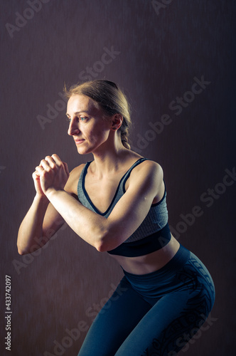The girl does squats. Physical exercises. Sports activities. Fototapeta