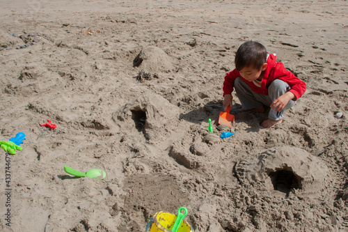 Little boy playing with the sand and sand toys at the beach. Boy building roads and tunnels with the sand. Pacific ocean. Outdoor summer activity. Horizontal, copy space.
