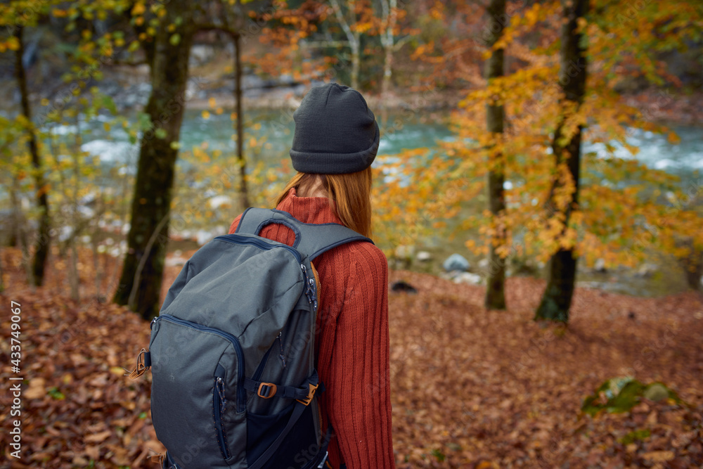 woman in a sweater with a backpack on her back near the river in the mountains and park trees autumn landscape