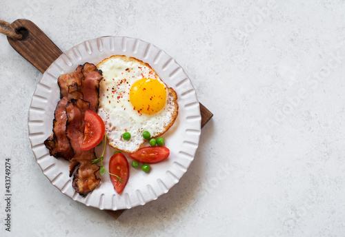 Fried egg, bacon and tomato on stone plate on gray stone background