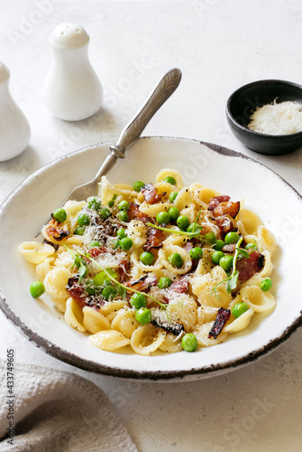 Pasta with fried bacon, green peas and parmesan cheese in rustic old plate