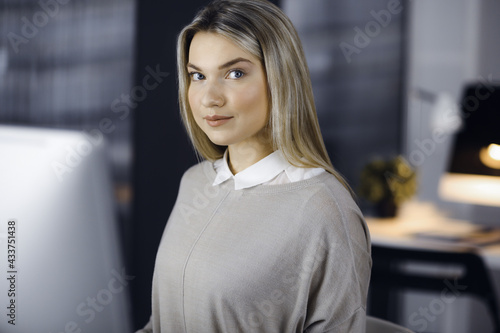 Blonde business woman sitting and looking at camera in office. Business headshot portrait