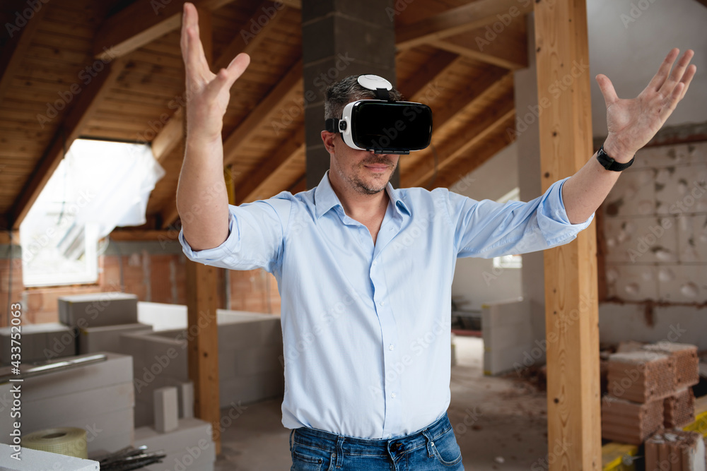 good looking male architect with virtual reality goggles and blue shirt on construction site in loft, attic good looking male architect with virtual reality goggles and blue shirt on construction site in loft, attic