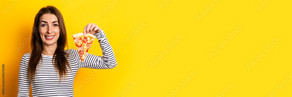 smiling young woman holding a slice of fresh pizza on a yellow background. Banner smiling young woman holding a slice of fresh pizza on a yellow background. Banner