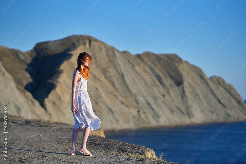 a traveler in a white dress walks in nature in the mountains near the sea