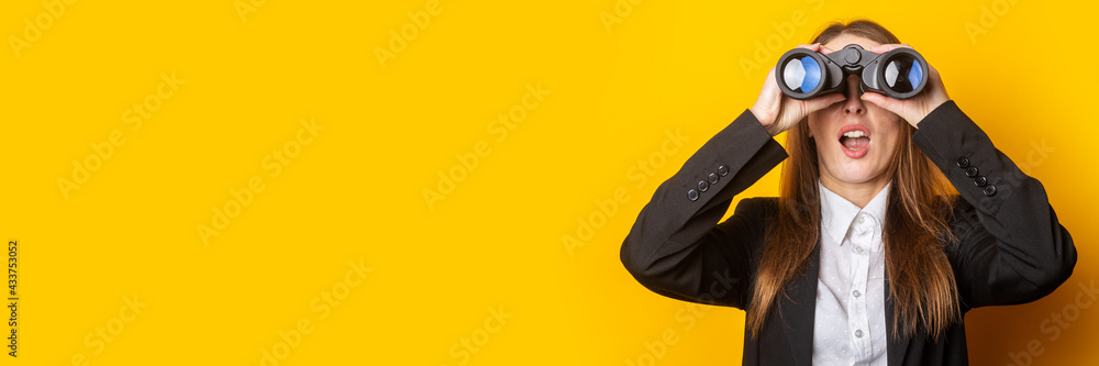 surprised young business woman looking through binoculars on yellow background - obrazy, fototapety, plakaty 