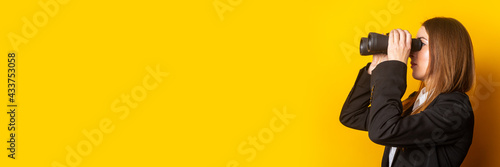 young business woman looking through binoculars on a yellow background. Banner photo