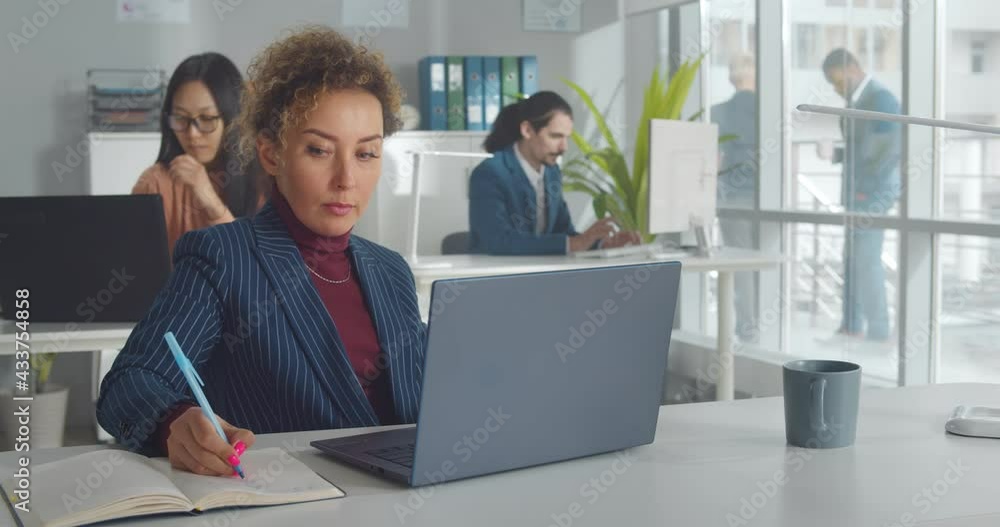 Confident multiethnic businesswoman with curly hair using laptop in office Confident multiethnic businesswoman with curly hair using laptop in office