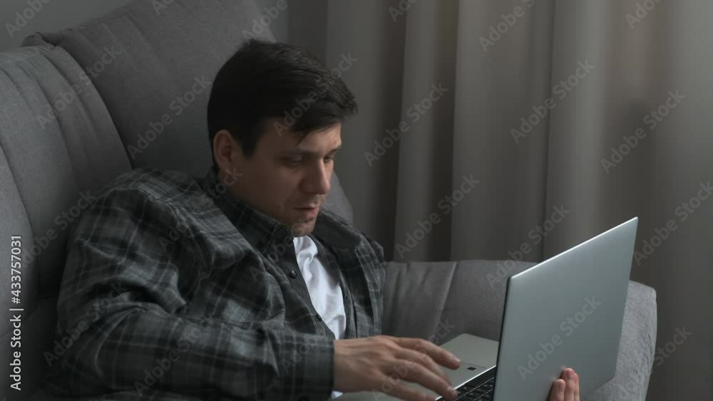 Thoughtful calm man is lying on comfortable couch, spending time online web surfing information, doing project research, working remotely on laptop from home, freelance workday lifestyle. Side view. Thoughtful calm man is lying on comfortable couch, spending time online web surfing information, doing project research, working remotely on laptop from home, freelance workday lifestyle. Side view.