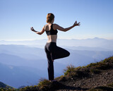 Back view of sporty woman doing yoga exercise and standing on one leg in mountains. Concept of harmony with nature.