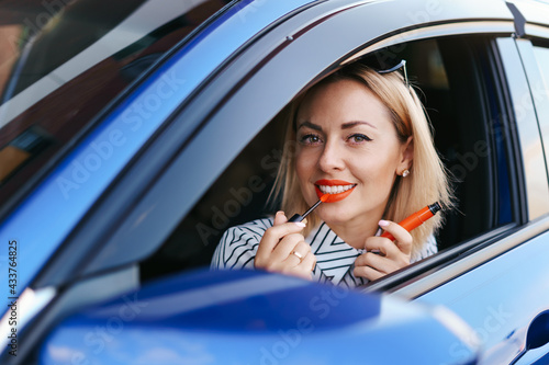 Young Caucasian woman applying lipstick looking at reflection in car mirror. photo