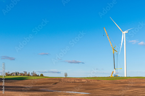 Wind turbine under construction near a village in a agricultural field with clear blue sky on background. Renewable energy concept, green ecological energy generation. Energy industry