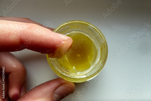 Gelbe Salbe in einem runden Glas wird von einem Finger prüfend entnommen. Zähflüssige gelbe leicht transparente Masse. Hamamelis-Salbe gegen Hämorrhoiden. Disgusting ointment with earwax.