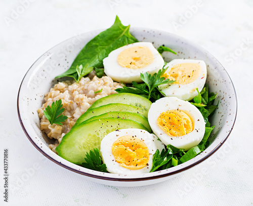 Breakfast oatmeal porridge with boiled eggs, cucumber and green herbs. Healthy balanced food.