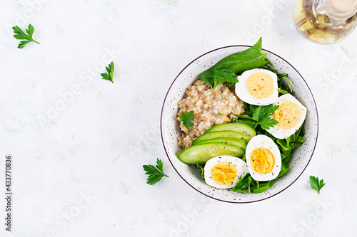 Breakfast oatmeal porridge with boiled eggs, cucumber and green herbs. Healthy balanced food. Top view, above