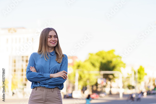 Shot of beautiful young businesswoman wearing blue chifon shirt while standing on the street with folded arms.