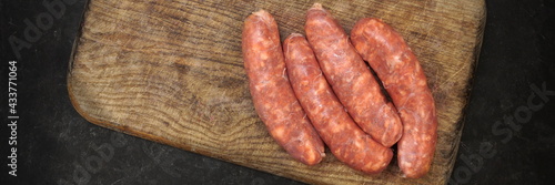 Raw Sausages In Natural Casing.  Stuffed Sausages on Old Wooden Cutting Board and Fork, Overhead View. Uncooked Sausages For Grilling or Frying on Wood Board And Black Table in Background, Top View.