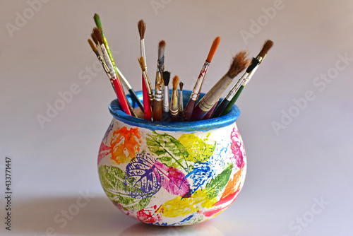 Artist's painting brushes in a painted pot, against white background.