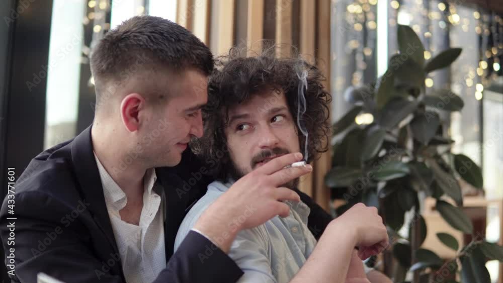 Happy gay couple having a romantic dinner in a restaurant, hugging and smoking a cigarette. Gay, LGBT, homosexuality love concept Happy gay couple having a romantic dinner in a restaurant, hugging and smoking a cigarette. Gay, LGBT, homosexuality love concept