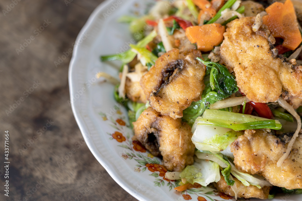 Stir-fried fish and vegetables in a plate placed on a wooden table. Stir-fried fish and vegetables in a plate placed on a wooden table.