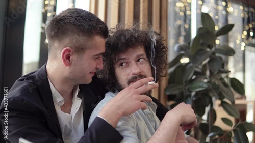 Happy gay couple having a romantic dinner in a restaurant, hugging and smoking a cigarette. Gay, LGBT, homosexuality love concept