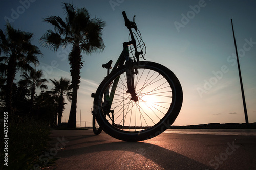 Silhouette of a bike at sunset. The sun shines through the bicycle wheel at the sea side park