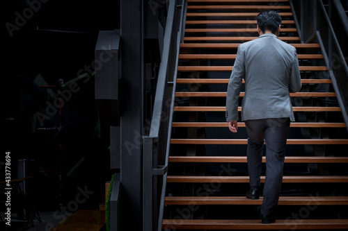 Back view of businessman walking up staircase, modern building. Copy space.