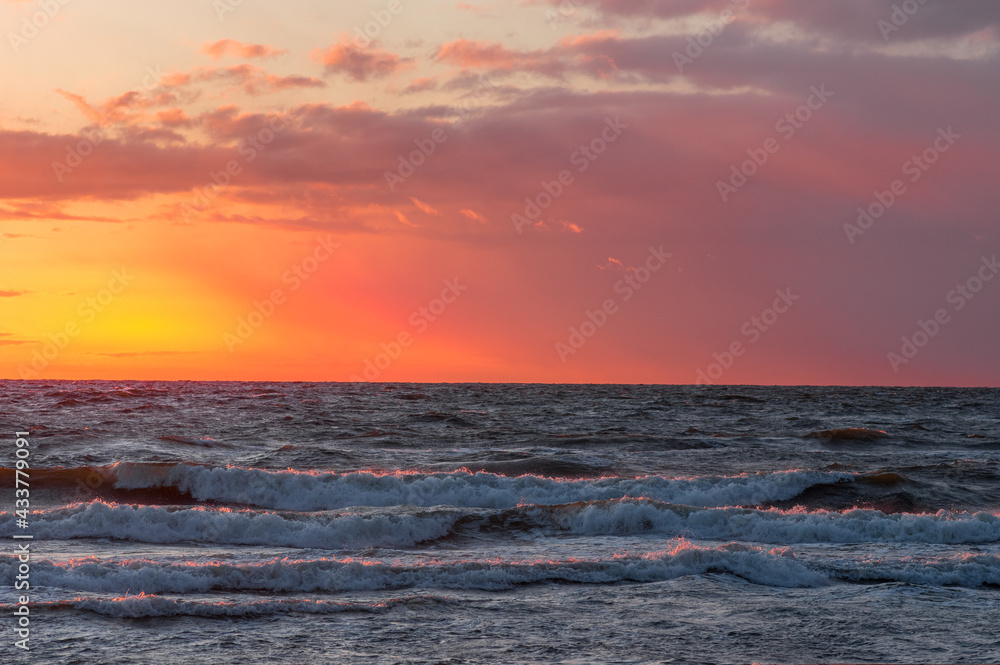 Stunning sunset reflections on the crashing sea waves. Red and orange background and light clouds.